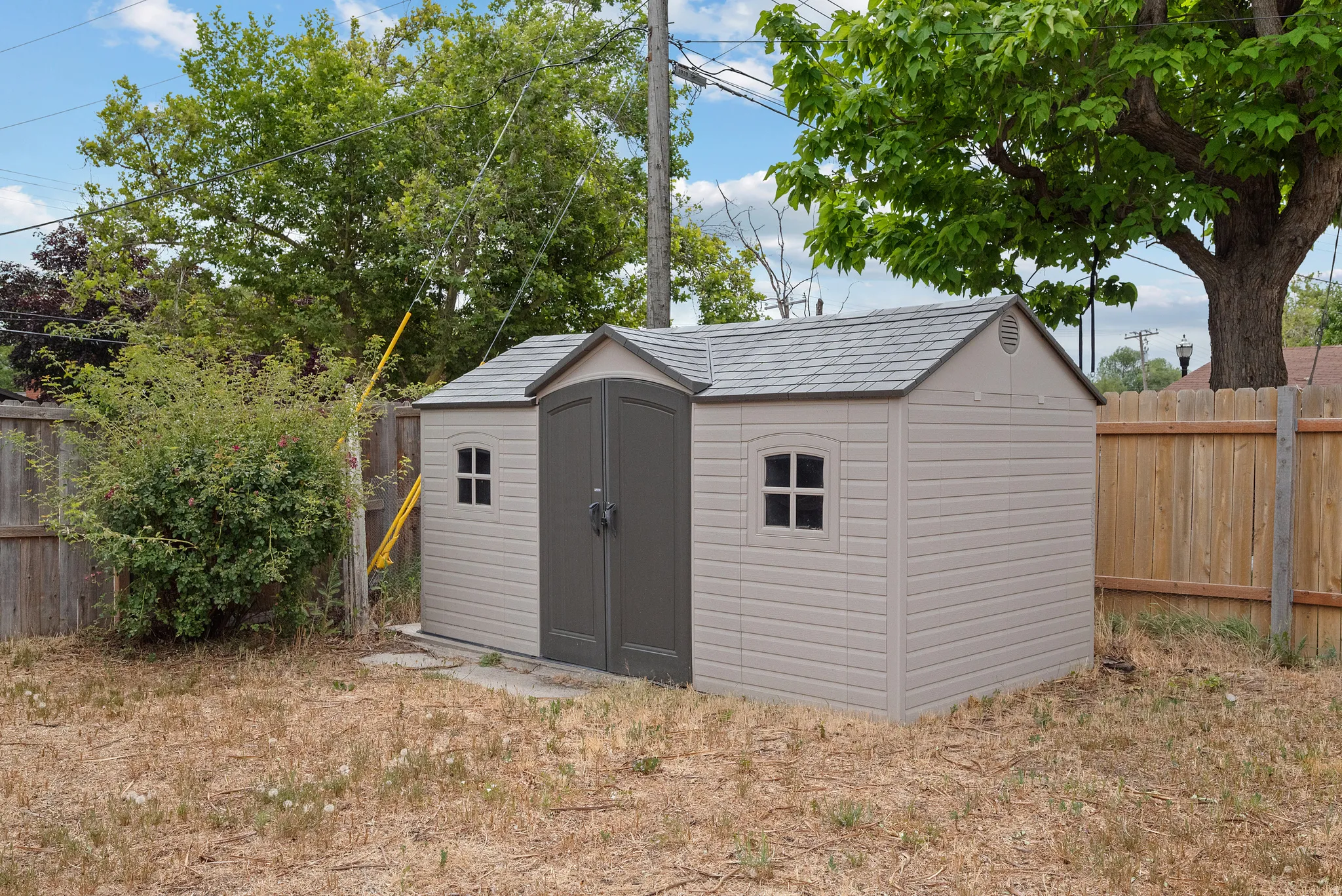 Freestanding outdoor shed featuring a shingled roof, double doors, and two fixed windows