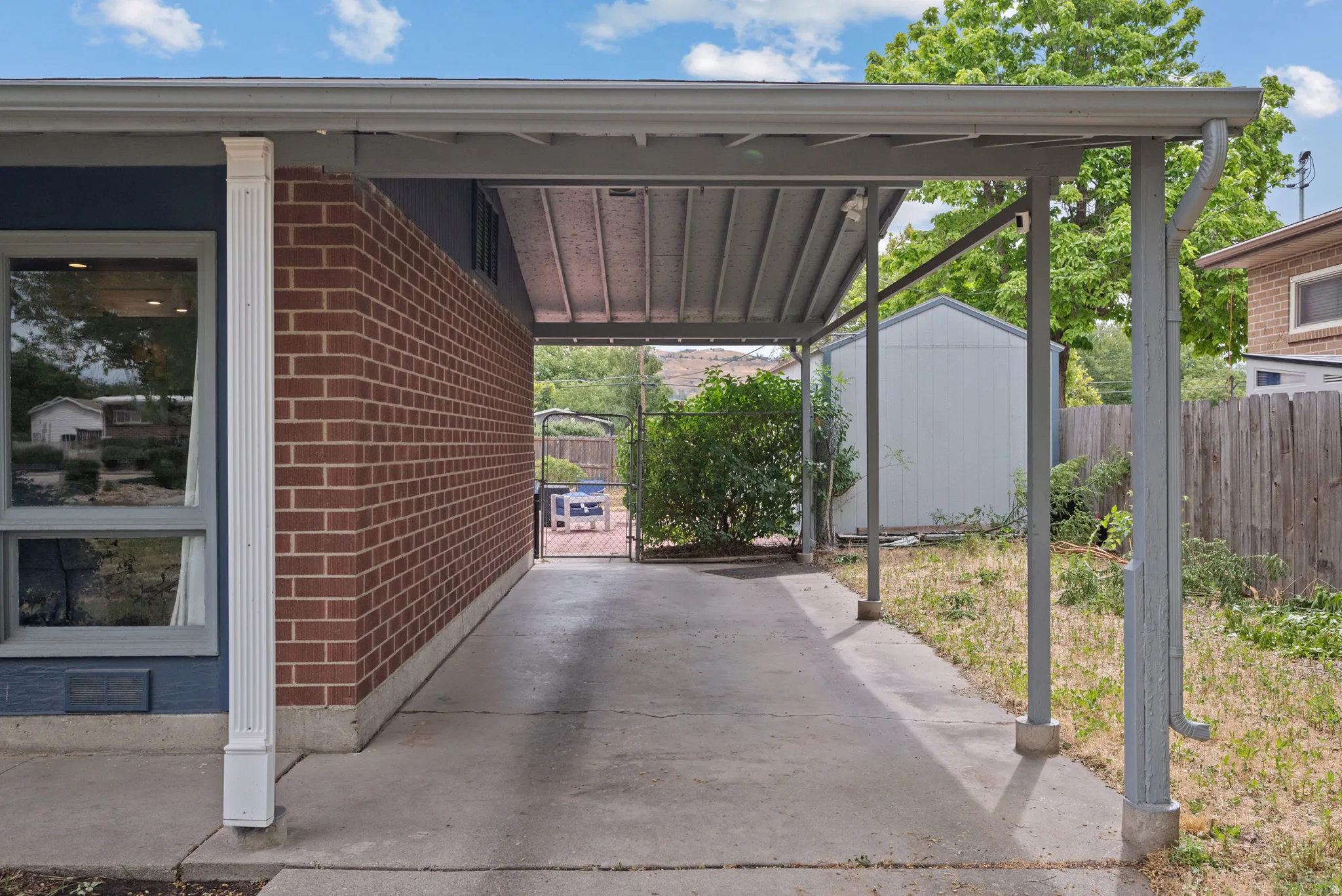 Covered carport area featuring a concrete drive, brick exterior wall, and a side window