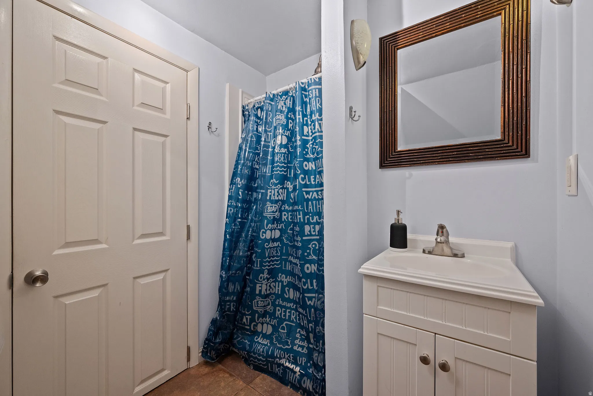 Bathroom featuring a white vanity with beadboard cabinetry and an integrated sink, a framed rectangular mirror, and a shower area