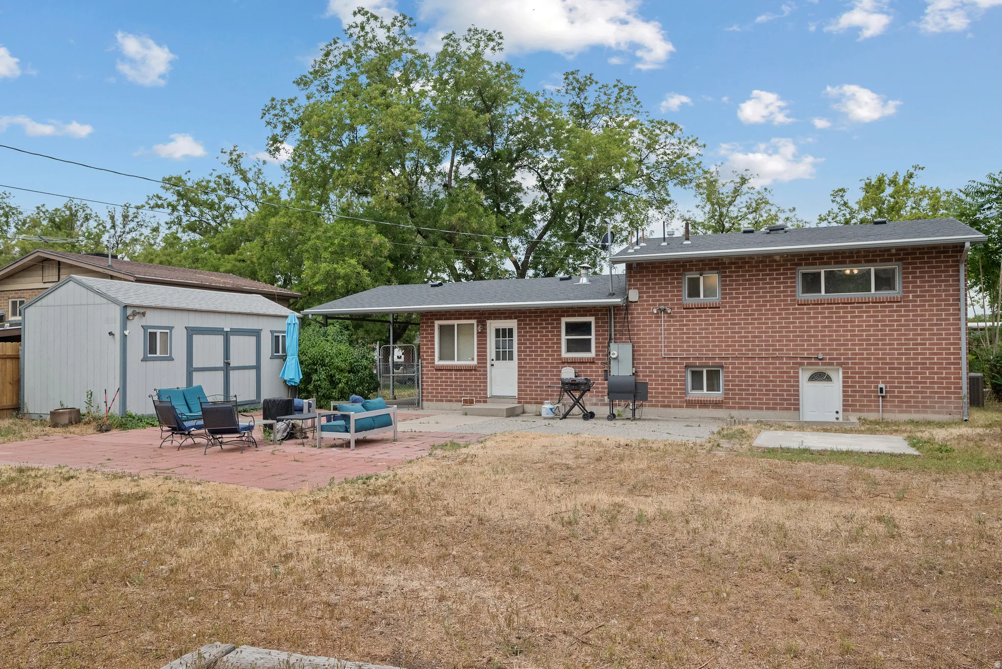 Spacious backyard featuring a brick exterior home, a large patio area with red pavers, a separate storage shed, an exterior door with direct outdoor access, and a covered back patio