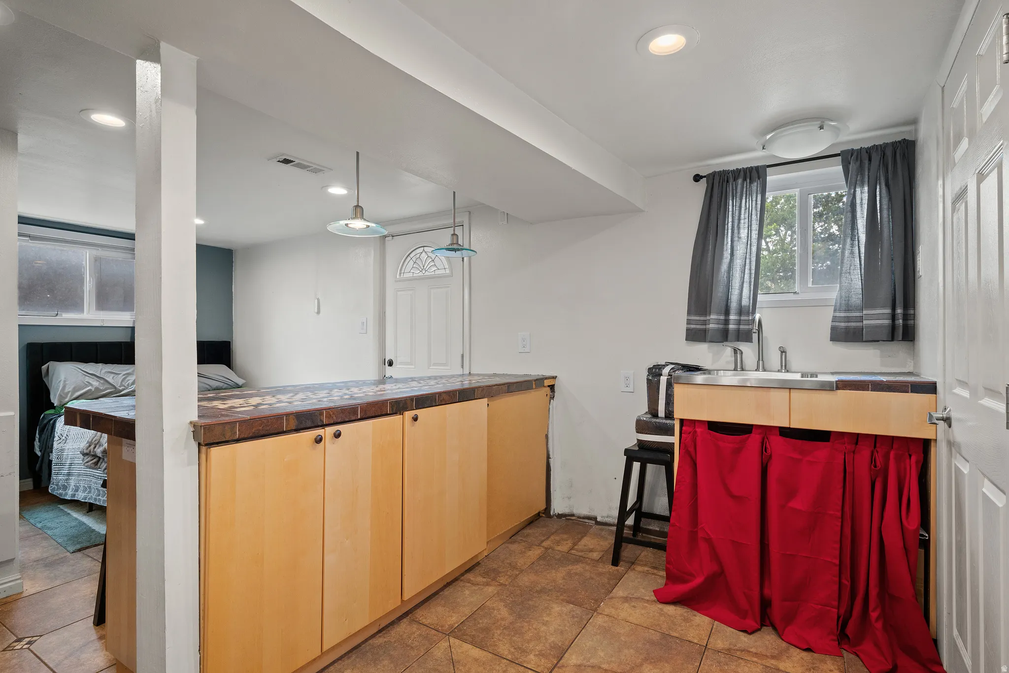 Kitchenette featuring wood-finish cabinetry, tile flooring, a stainless steel sink, and overhead pendant lighting