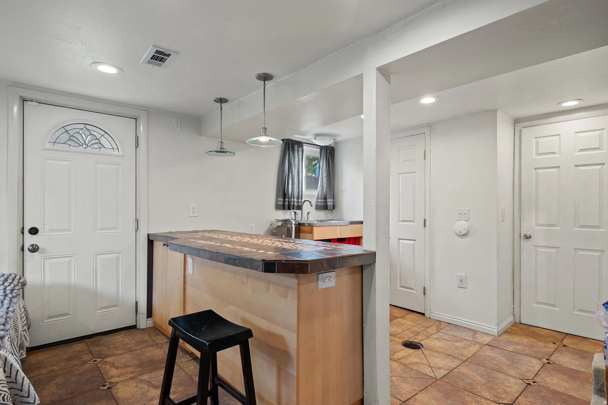 Kitchenette featuring a light wood-finish island with a dark countertop, two pendant lights, and recessed ceiling lighting