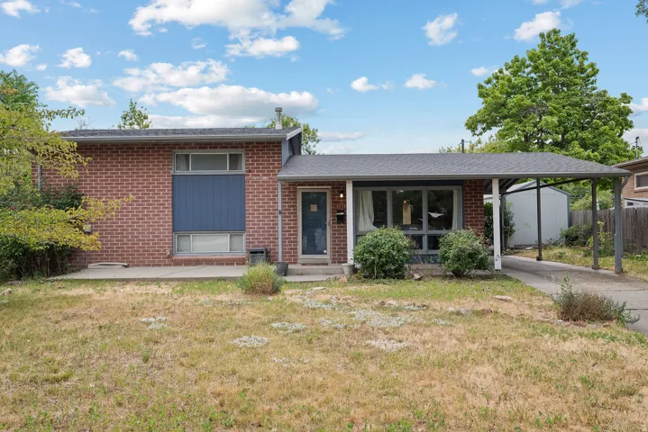Brick facade residence featuring a covered carport, pitched roofline, expansive front windows, and a concrete patio
