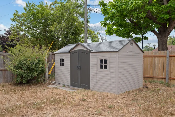 Freestanding outdoor shed featuring a shingled roof, double doors, and two fixed windows