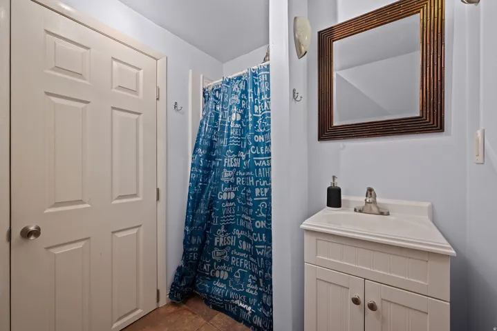 Bathroom featuring a white vanity with beadboard cabinetry and an integrated sink, a framed rectangular mirror, and a shower area