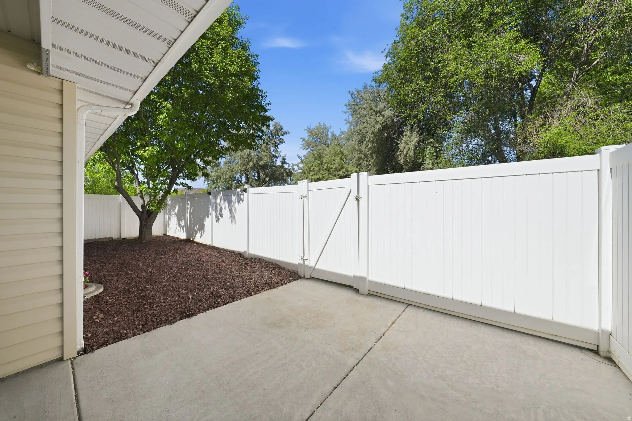Outdoor concrete patio extending to a white privacy fence with a sliding gate