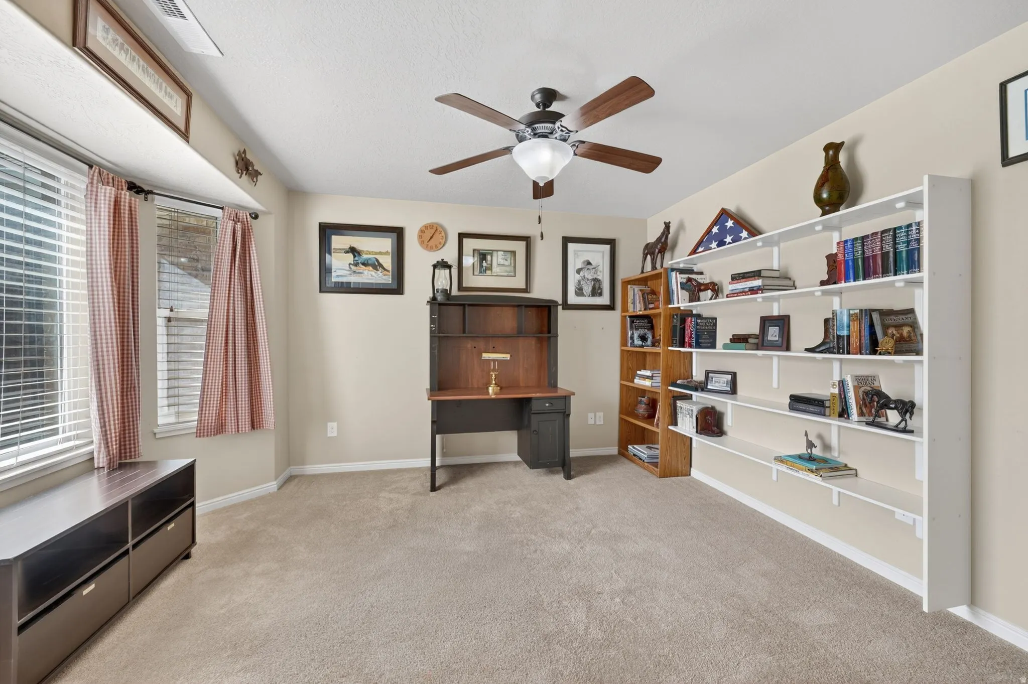 Carpeted room with multiple windows featuring blinds, a ceiling fan, and extensive built-in shelving