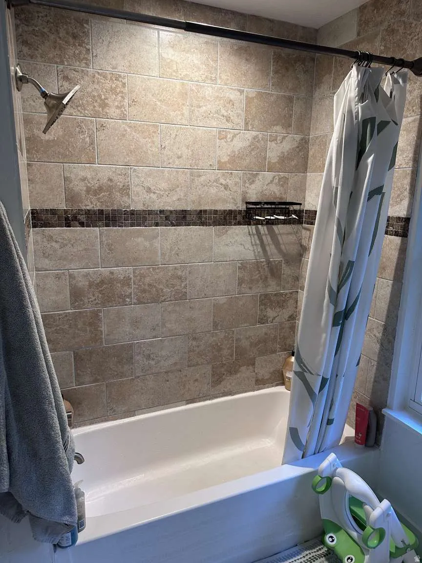 Bathtub and shower enclosure featuring full-height tile surround, decorative mosaic tile accent band, recessed shower caddy, and a fixed shower head