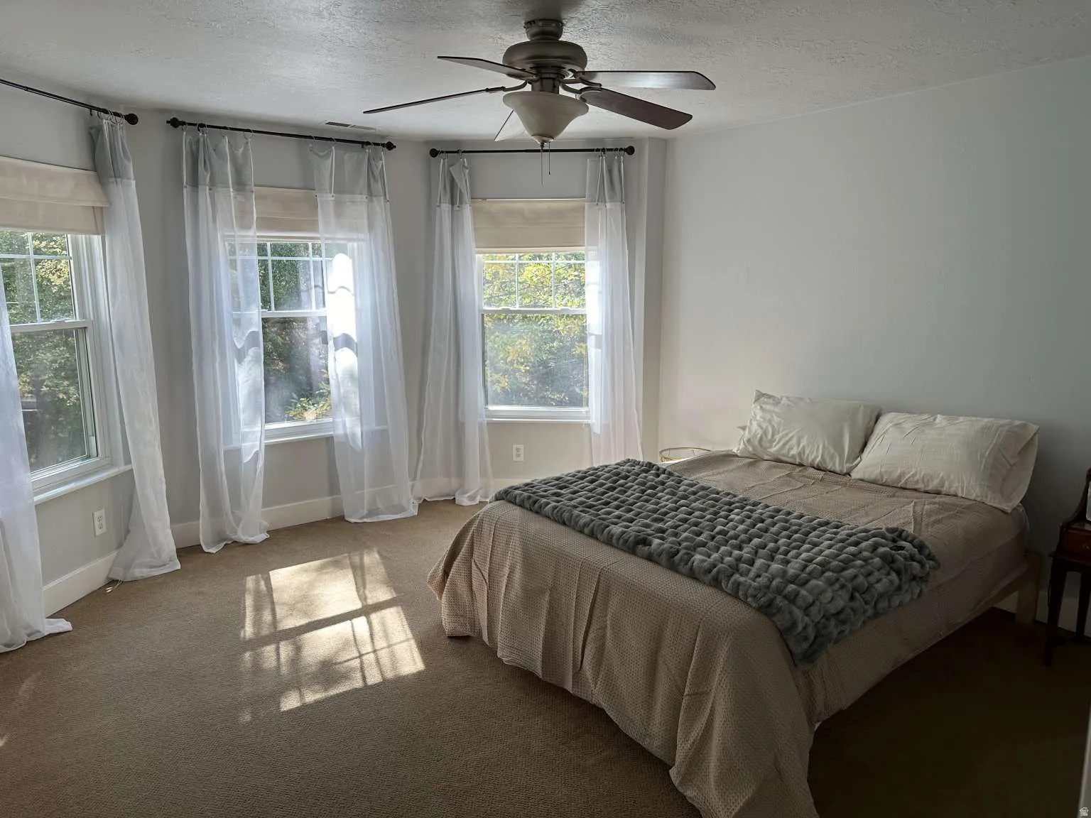Bedroom featuring a ceiling fan with integrated lighting, multiple windows, and neutral carpeting