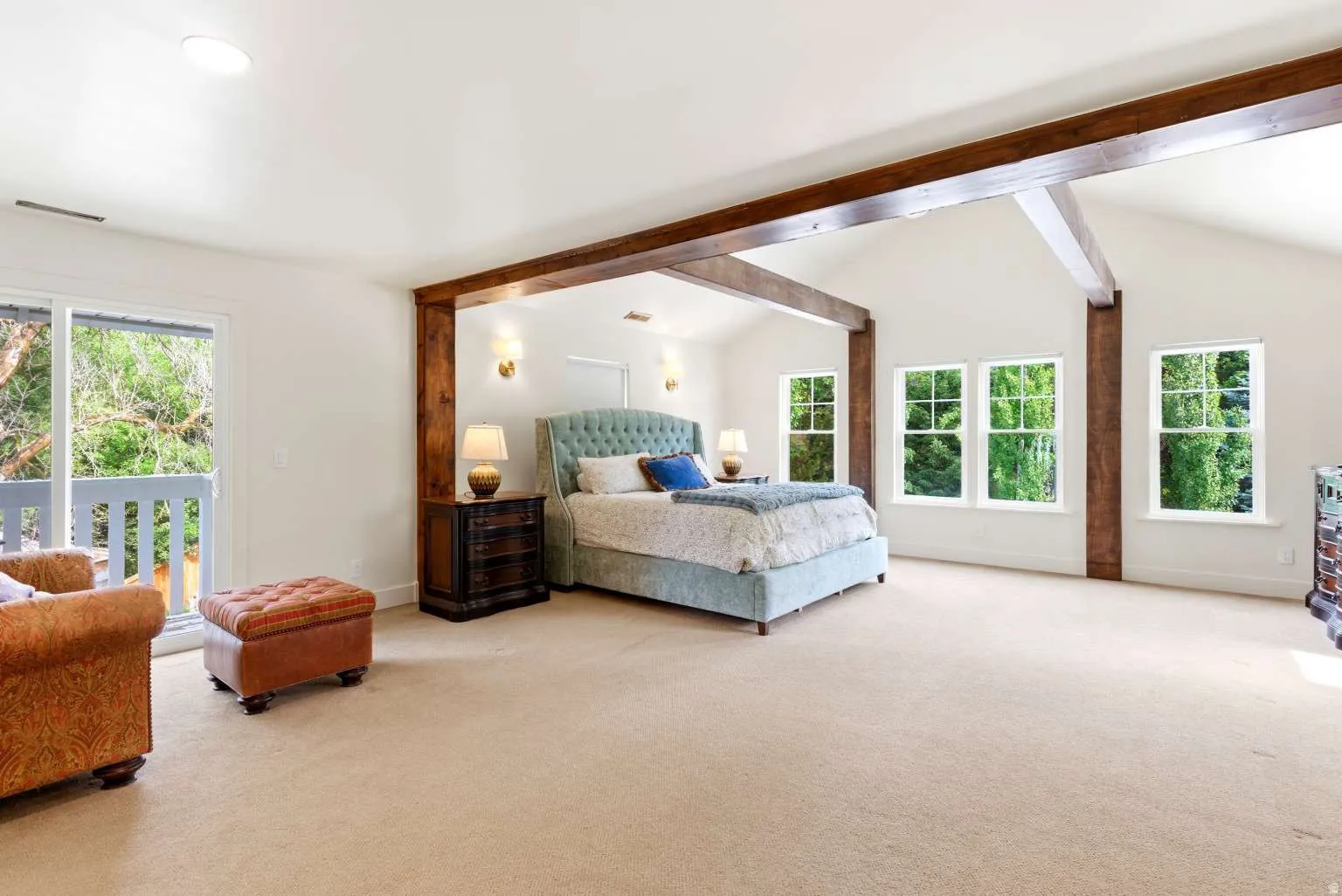 Spacious room featuring vaulted ceilings with exposed wood beams, light-toned carpeting, and a private balcony with white railings