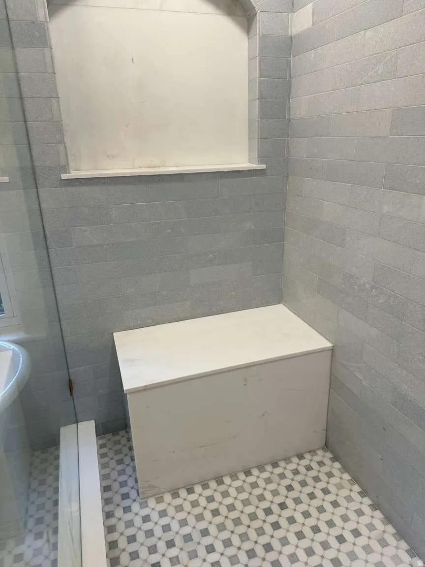 Shower stall featuring light gray subway tile walls and a decorative mosaic tile floor