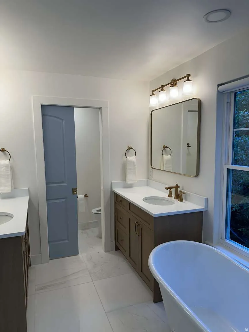 Bathroom featuring dual vanities with white countertops, a freestanding tub, and a pocket door leading to a water closet
