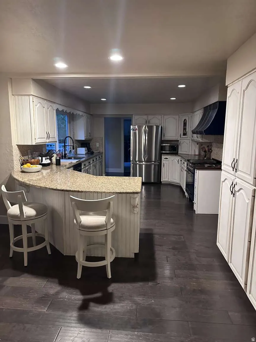 Expansive kitchen featuring wood-finish flooring, white cabinetry, a large kitchen island with a granite countertop, and stainless steel appliances