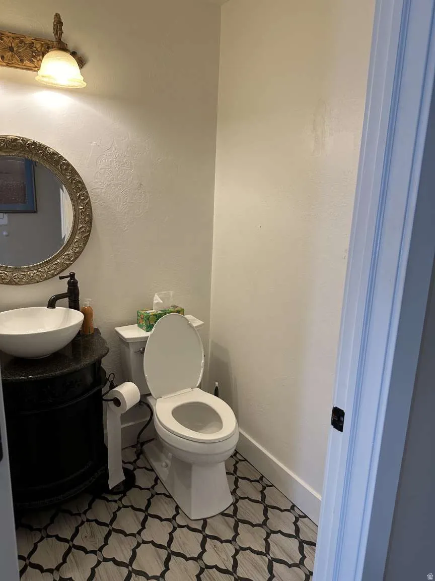 Powder room featuring a white vessel sink, black vanity with a stone-finish countertop, decorative wall mirror, and patterned floor tile