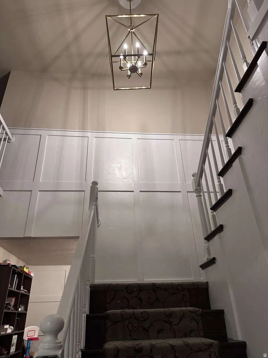 Two-story entryway featuring wainscoting, an ornate chandelier, and a carpeted staircase with white balusters