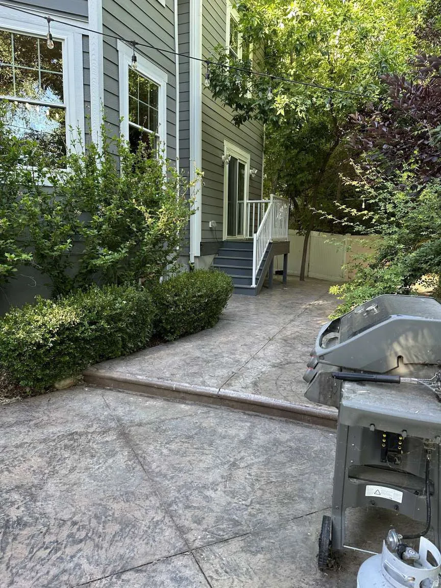 Exterior side of the property featuring gray horizontal siding, white trim, and a stamped concrete patio
