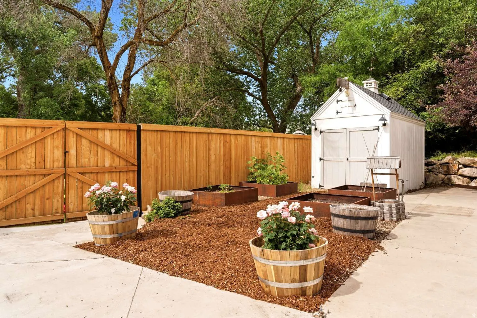 Dedicated garden area featuring a white storage shed with black hardware, several raised planters, and wood chip ground cover
