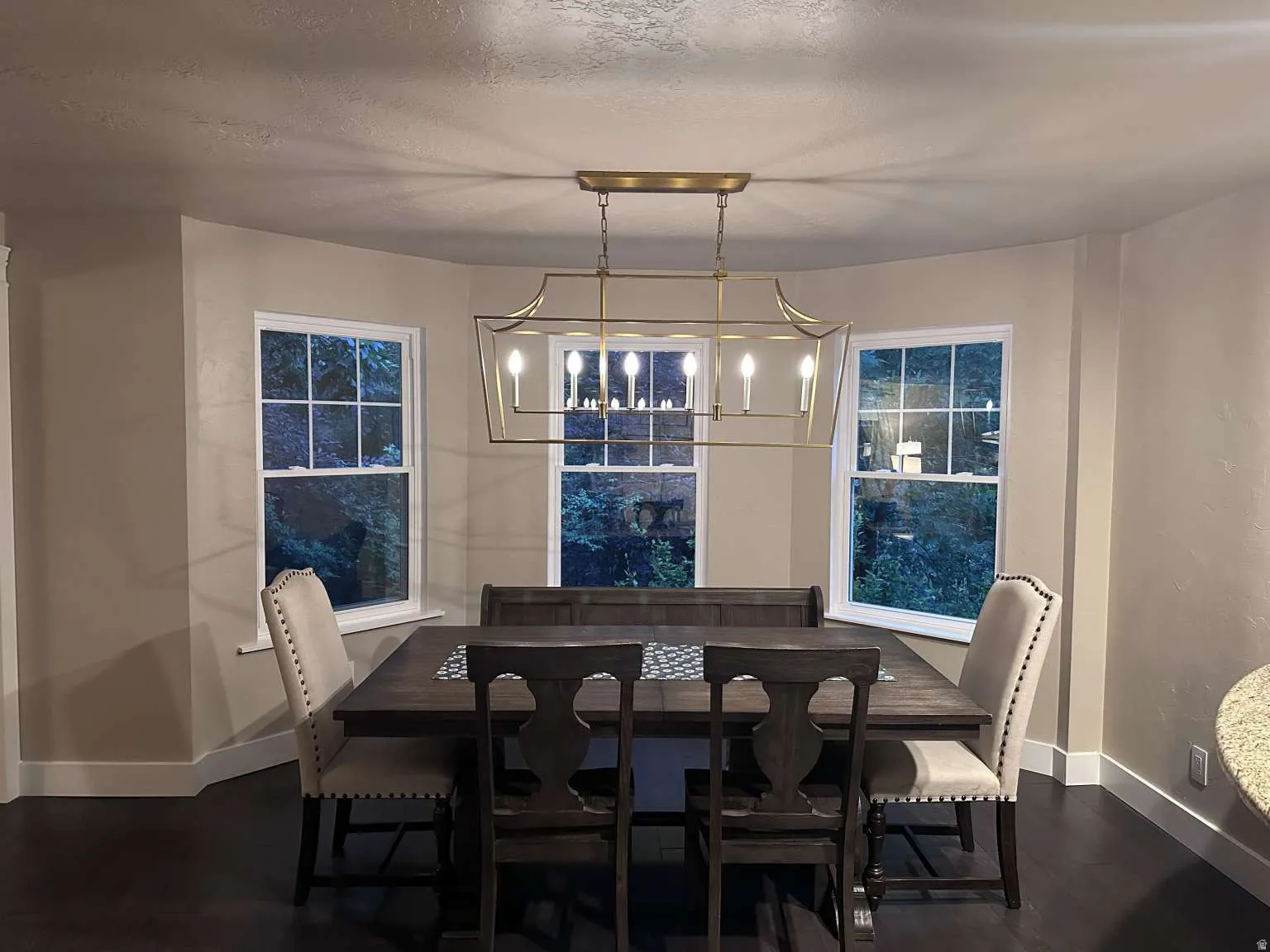 Dining area featuring dark wood-finish flooring, light tan walls, and a bay window configuration with three double-hung windows