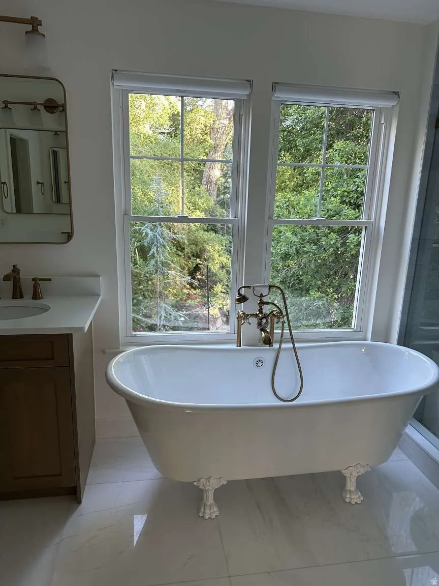 Freestanding clawfoot tub with brass fixtures and an adjacent vanity featuring a white countertop and wood-finish cabinetry