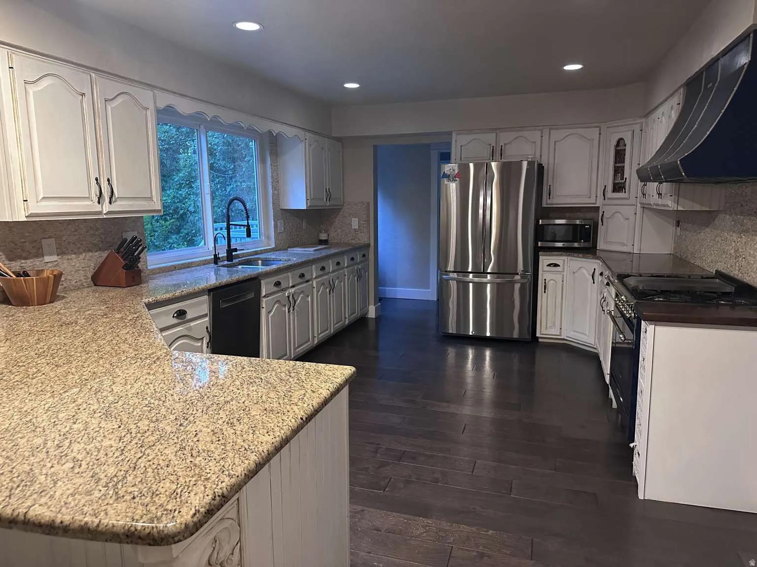Spacious kitchen featuring extensive counter space with granite countertops, light-toned cabinetry, dark wood-finish flooring, and recessed lighting