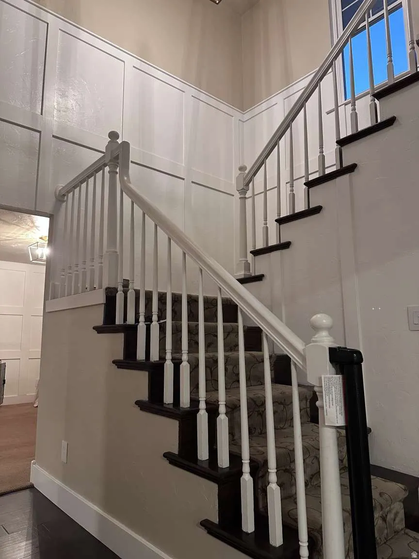 Grand staircase featuring dark wood treads with a patterned runner, white balusters, and a matching handrail