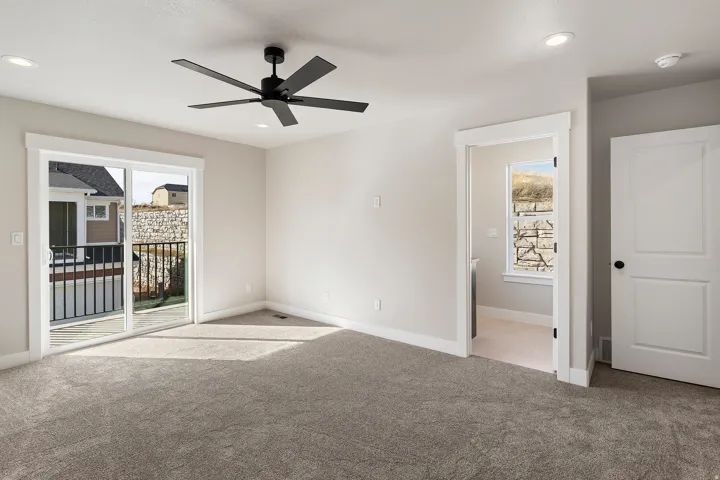 Carpeted room featuring a modern black ceiling fan, recessed lighting, and a sliding glass door providing direct outdoor access to a balcony with black metal railings