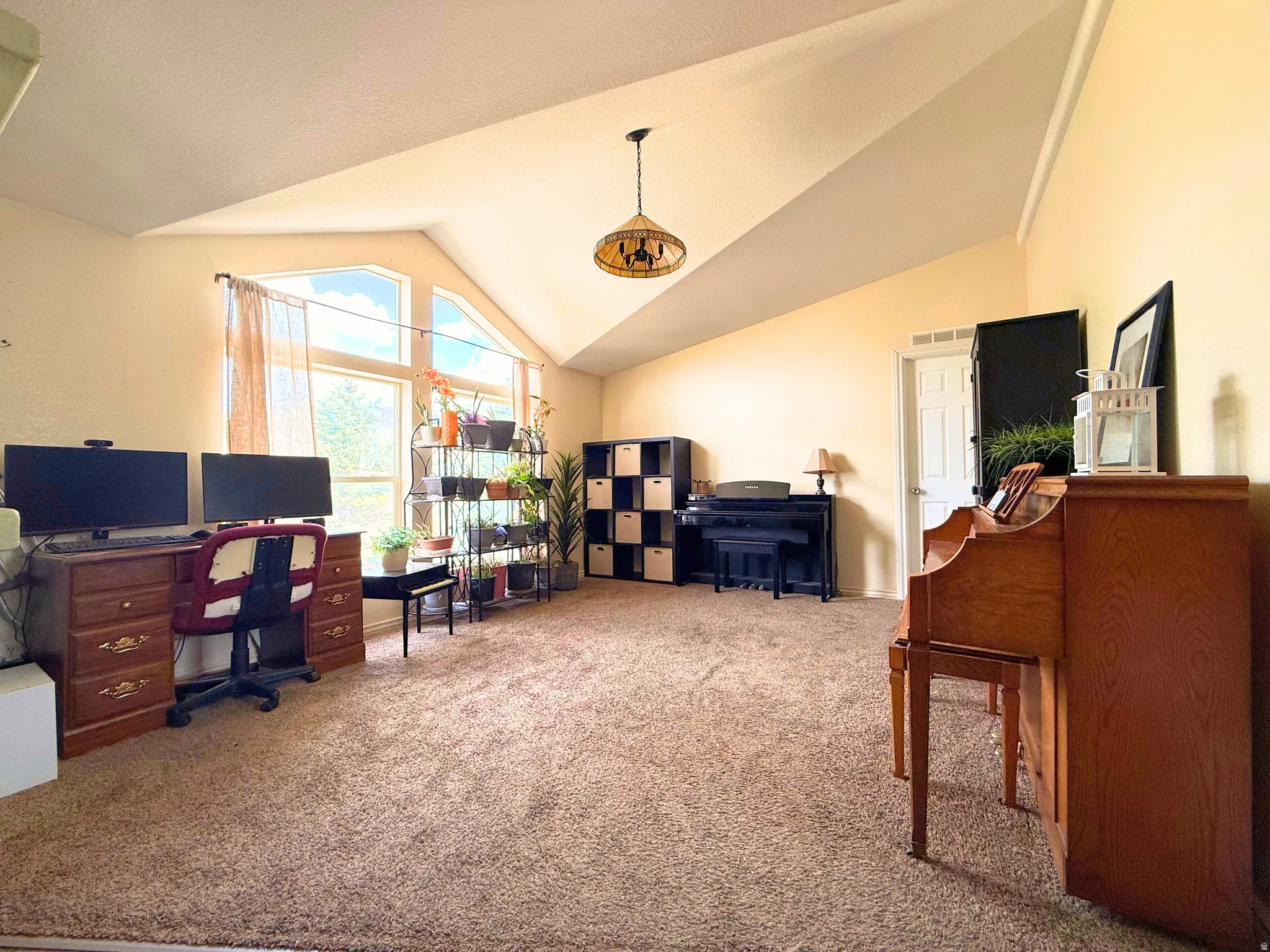 Spacious room featuring vaulted ceilings, a prominent window array, and neutral carpet flooring