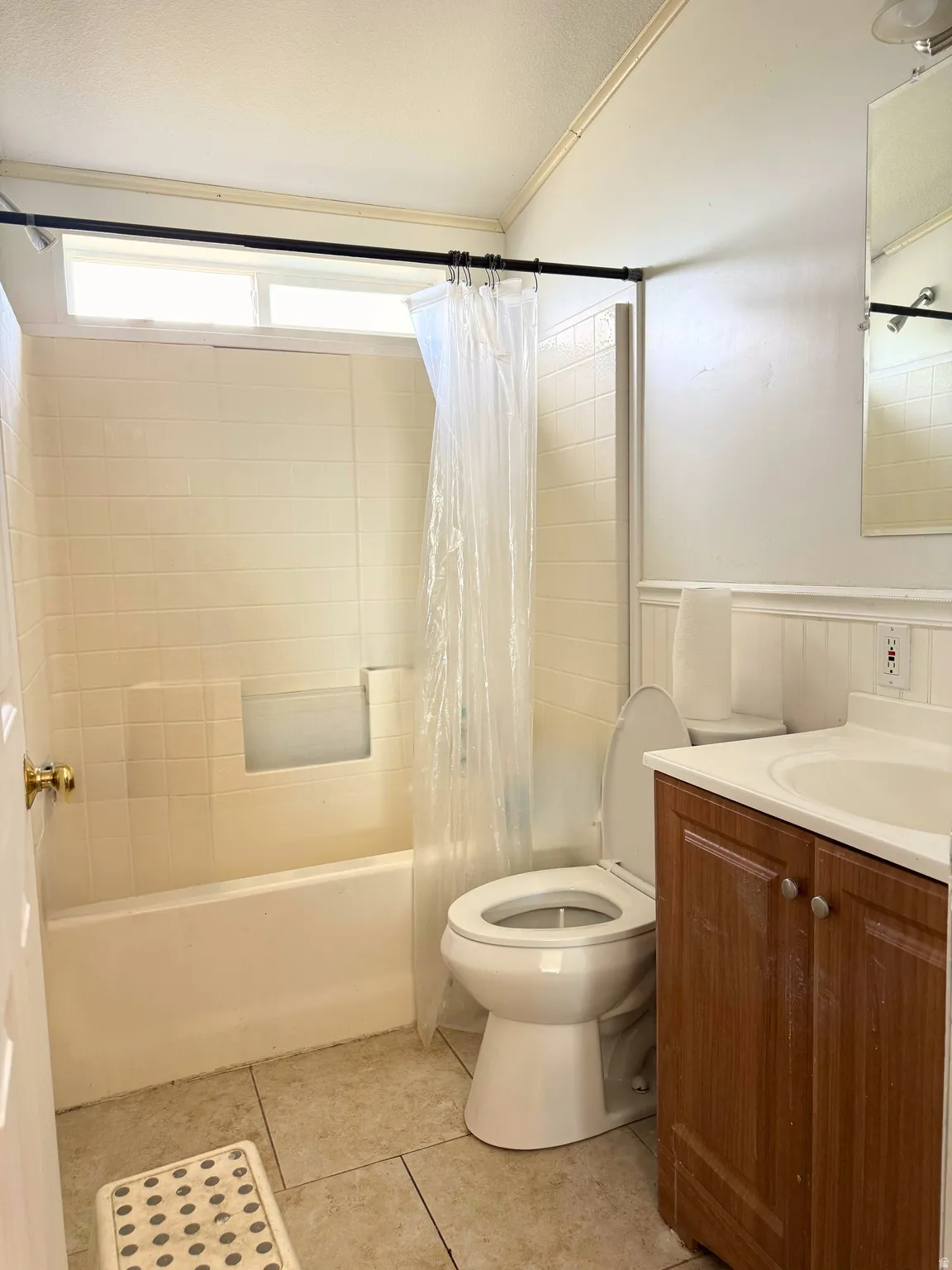 Bathroom featuring a white bathtub, ceramic tile flooring, a window above the tub, a vanity with a wood-finish cabinet, and a white toilet