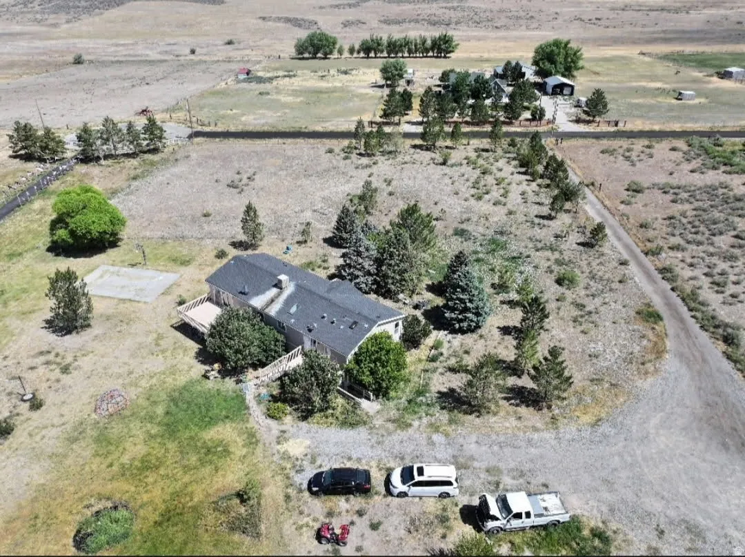 Spacious property featuring a single-story residence with a dark roof and chimney, multiple mature trees, and an expansive gravel driveway