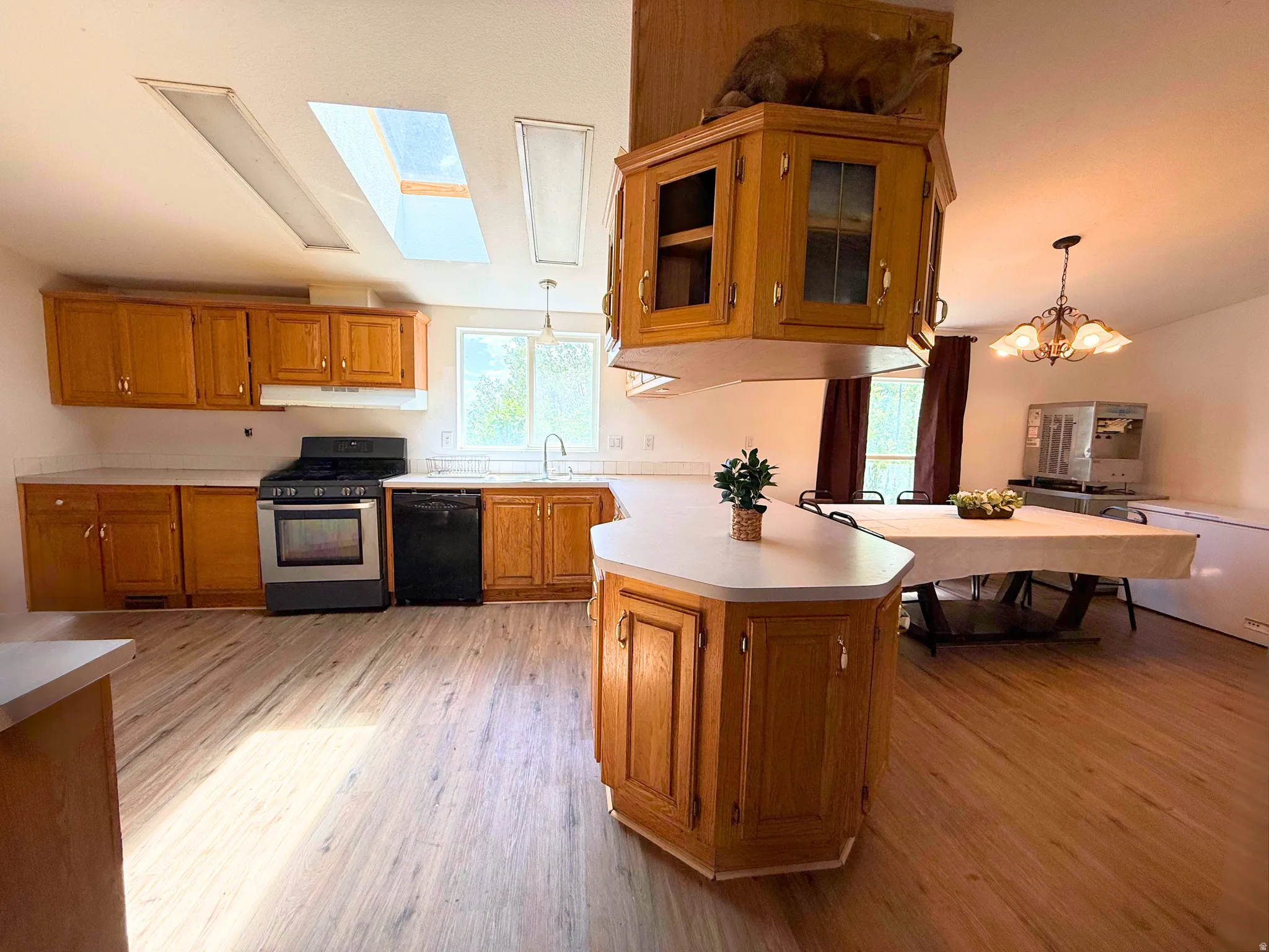 Open-concept kitchen featuring wood-finish flooring, light wood cabinetry, white countertops, and stainless steel appliances