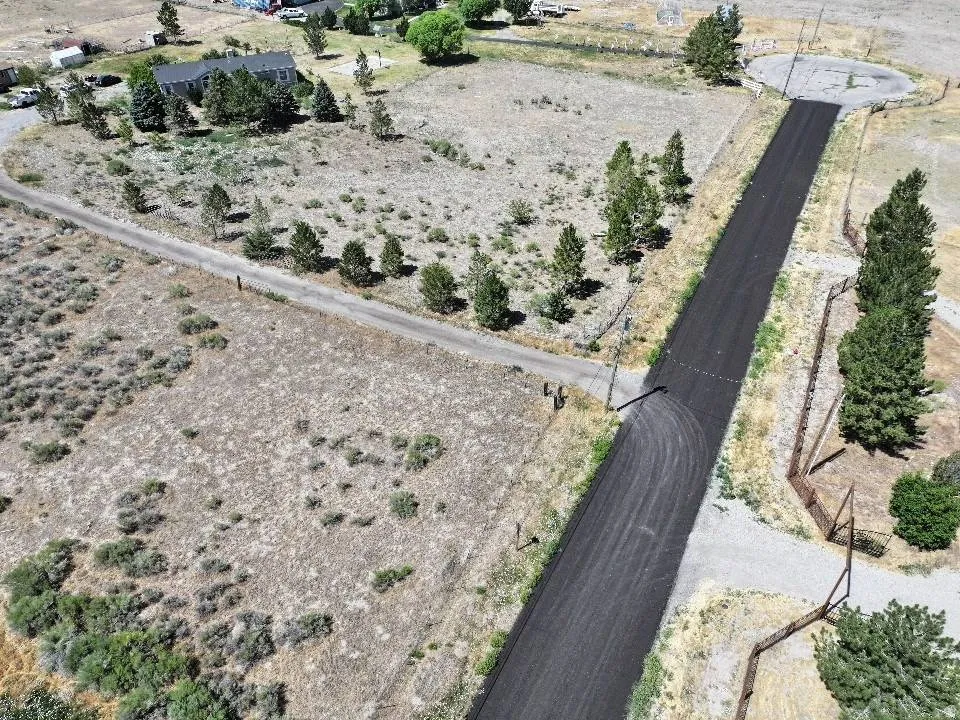 Paved road with a cul-de-sac turn-around, surrounded by undeveloped land and sparse trees