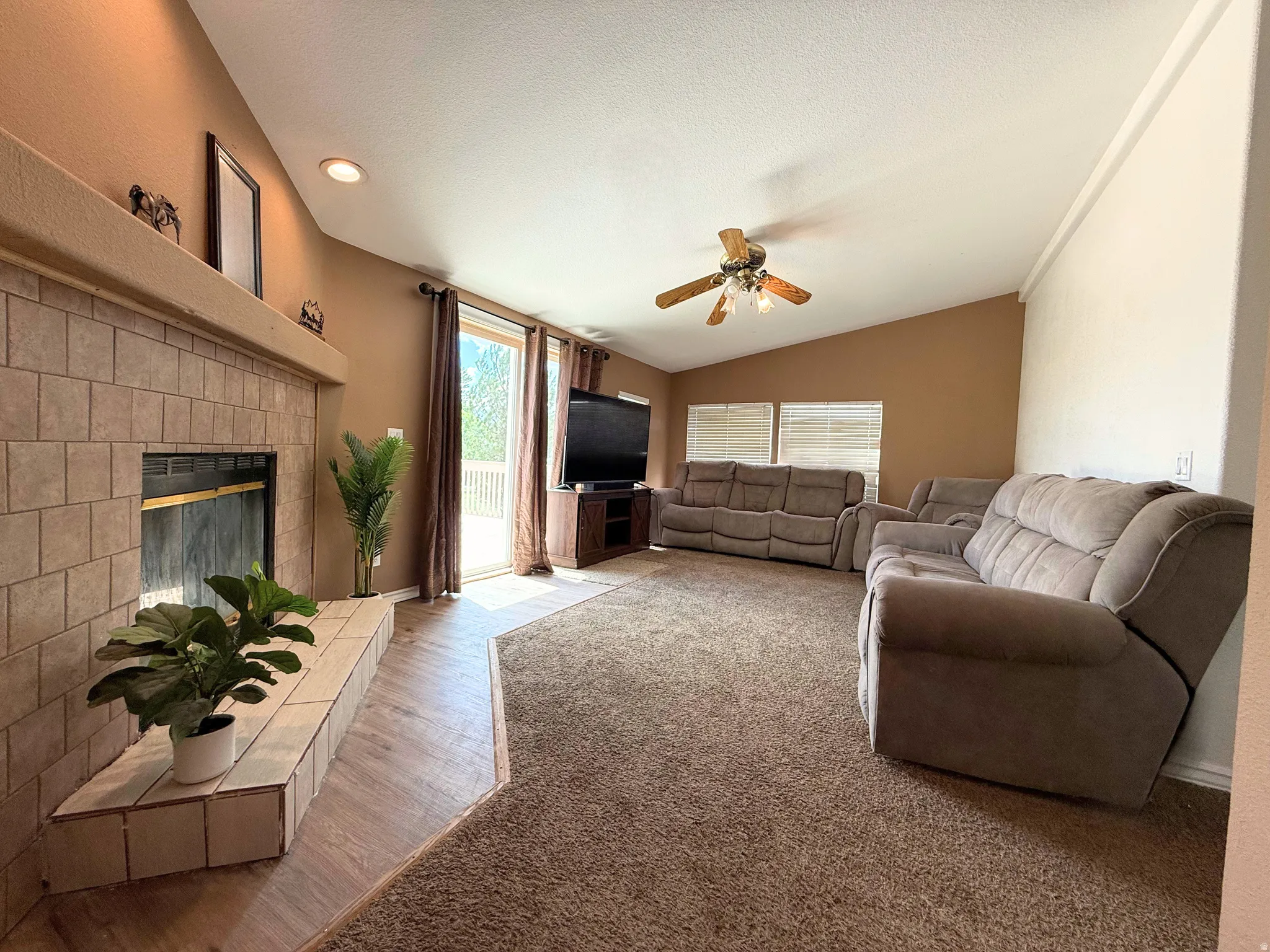 Spacious living area featuring a tile-surround fireplace with hearth, vaulted ceilings, and a ceiling fan