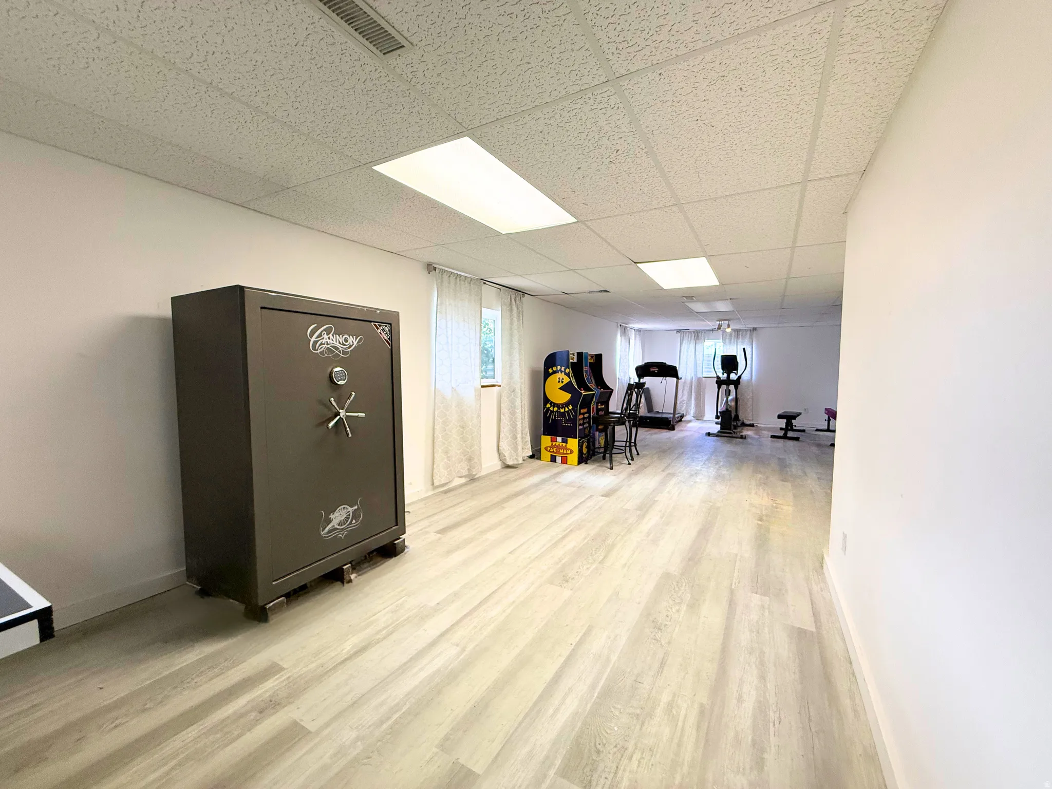 Spacious room featuring light wood-finish flooring, white walls, and a drop ceiling with integrated lighting