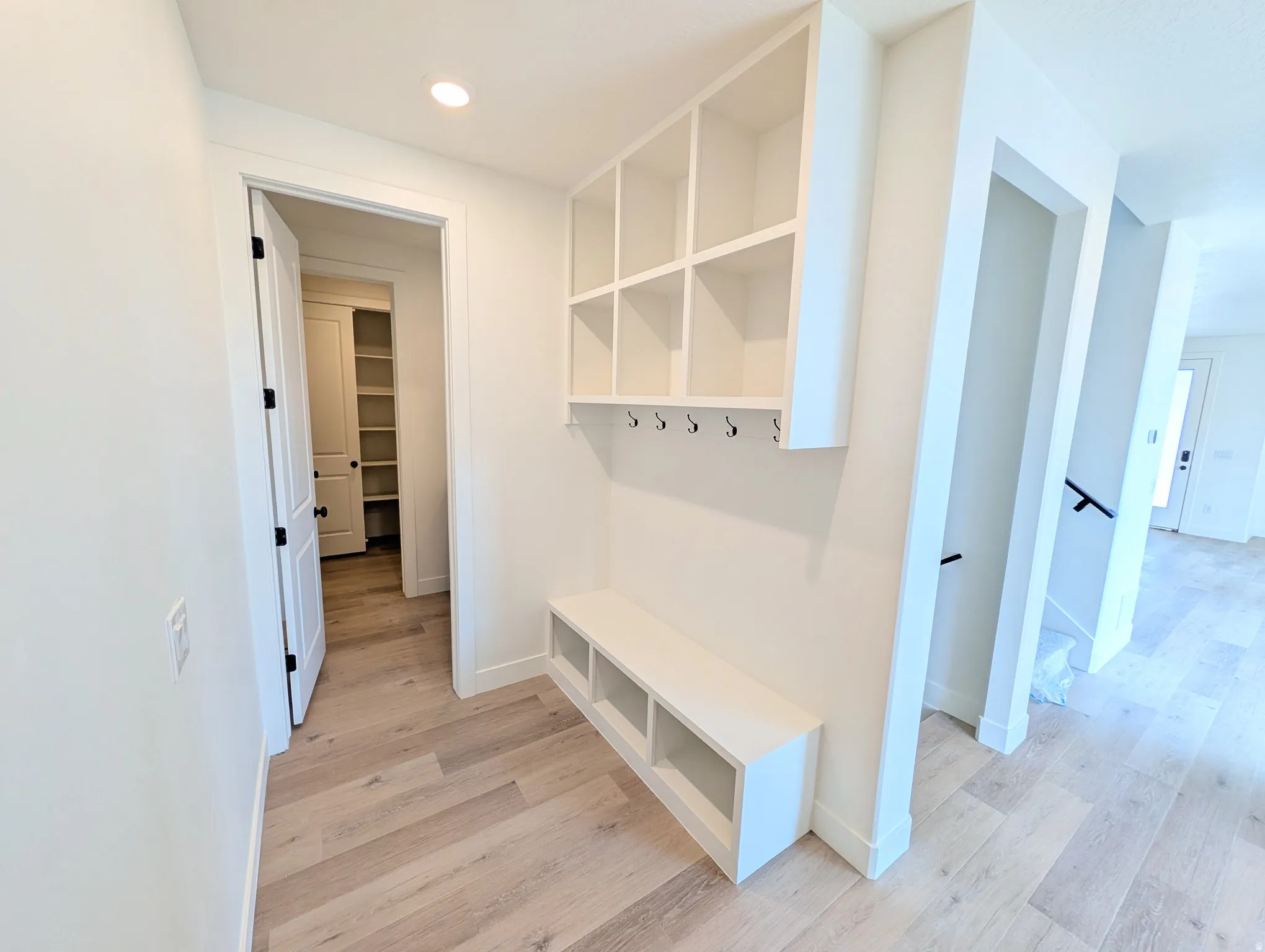 Entryway mudroom featuring built-in white cabinetry, integrated bench seating, black coat hooks, and wood-finish flooring
