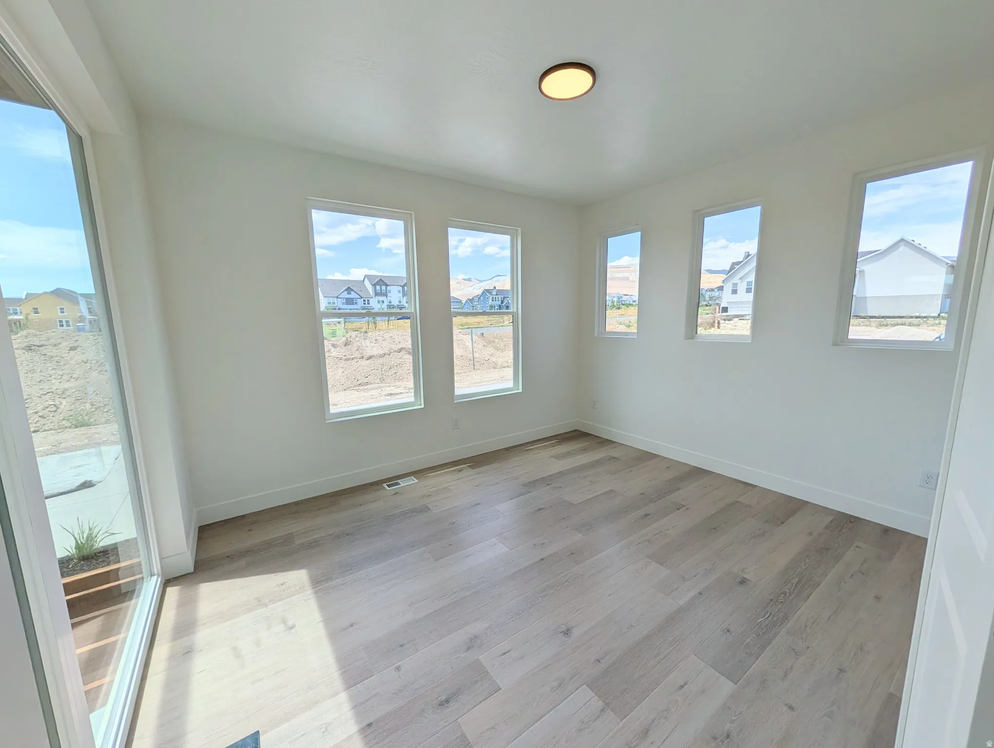 Bright interior space with wood-finish flooring, white baseboards, and multiple windows