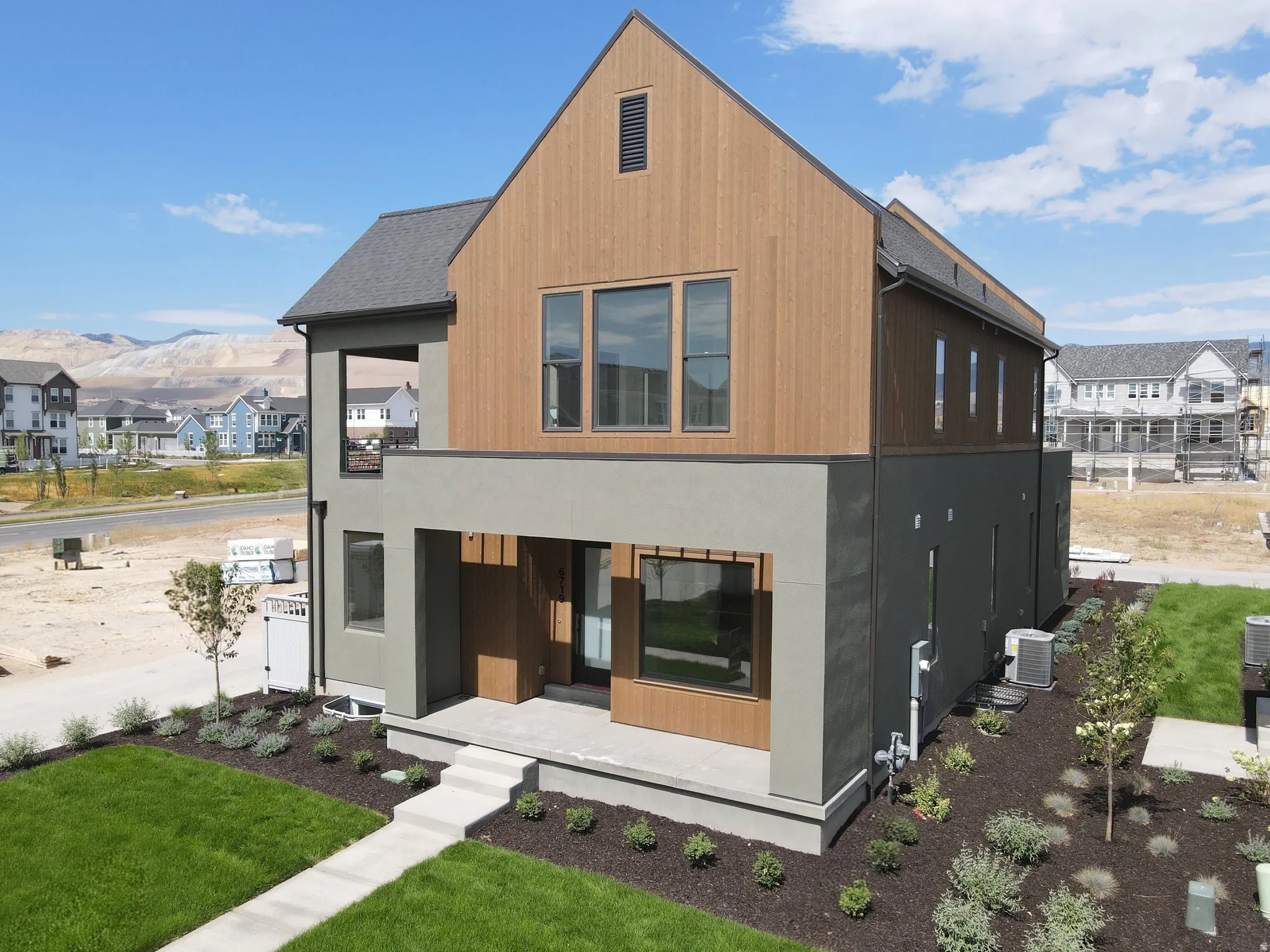 Contemporary two-story residence featuring a striking combination of wood-finish siding, dark grey paneling, and light stucco