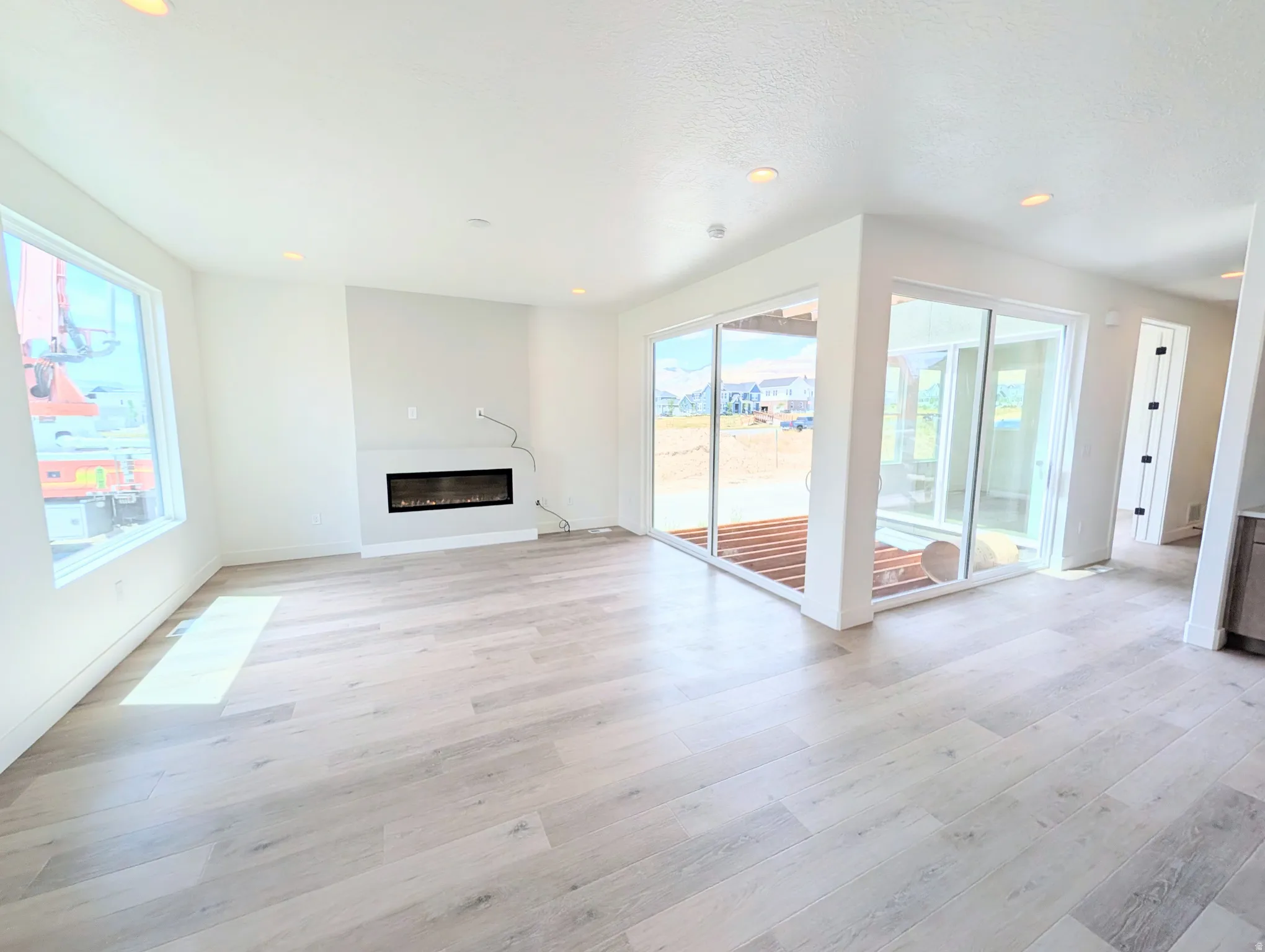 Spacious room featuring light wood-finish flooring, recessed lighting, and a built-in linear electric fireplace