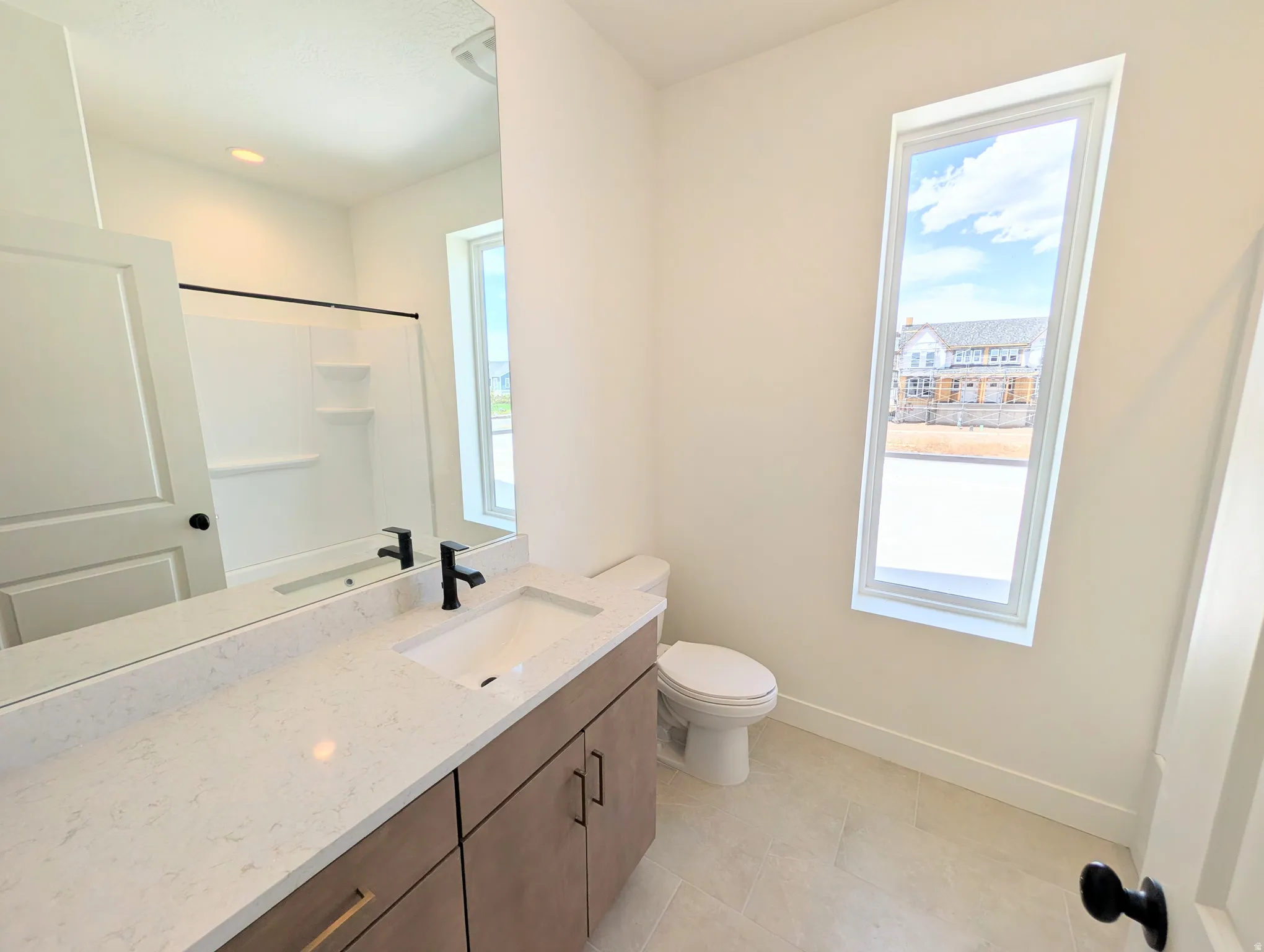 Bathroom featuring a vanity with an integrated rectangular sink and quartz countertop, wood-finish cabinetry with matte black hardware, and an elongated window