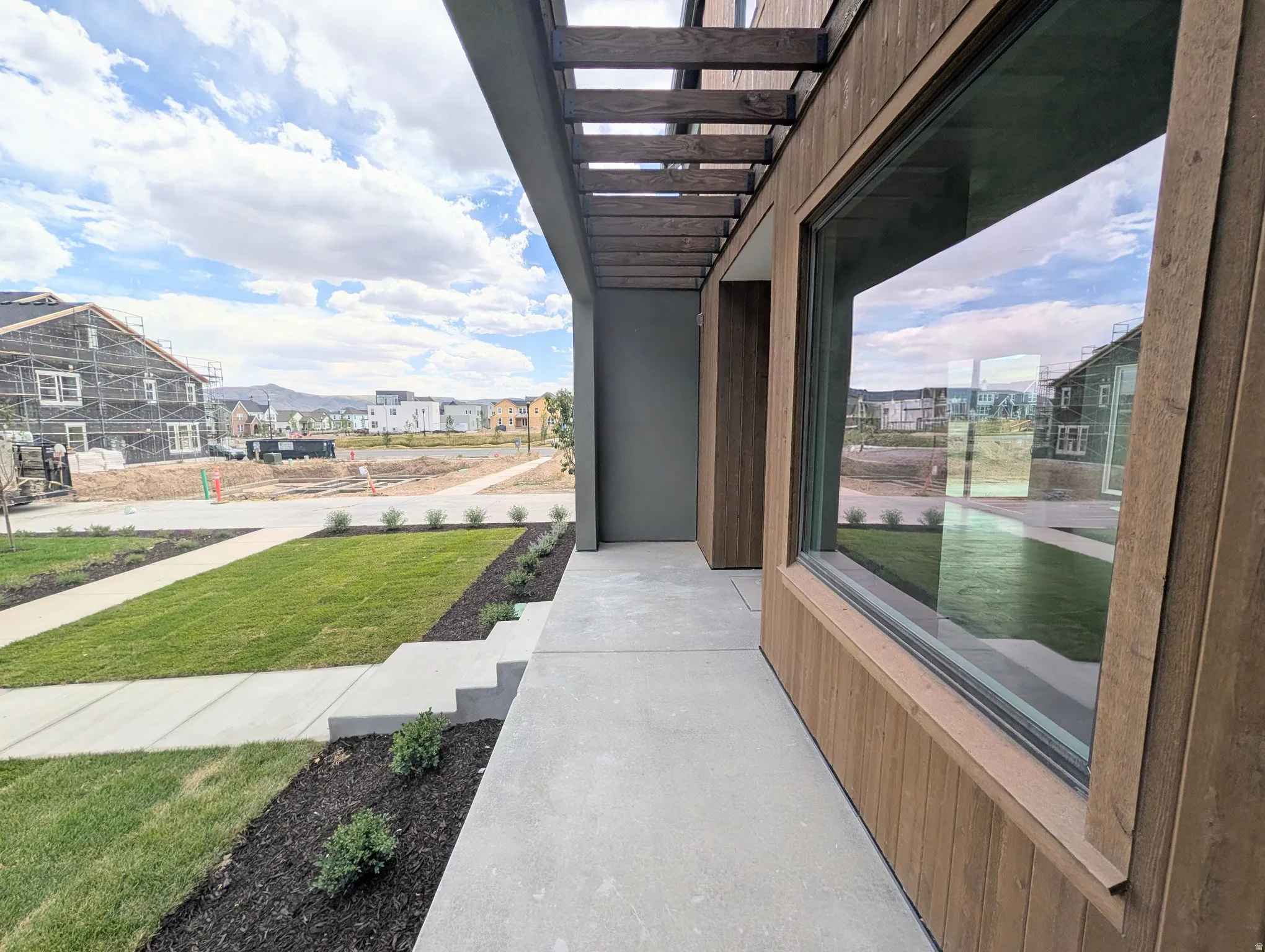 Modern exterior featuring wood-finish siding, a large picture window, and an overhead trellis