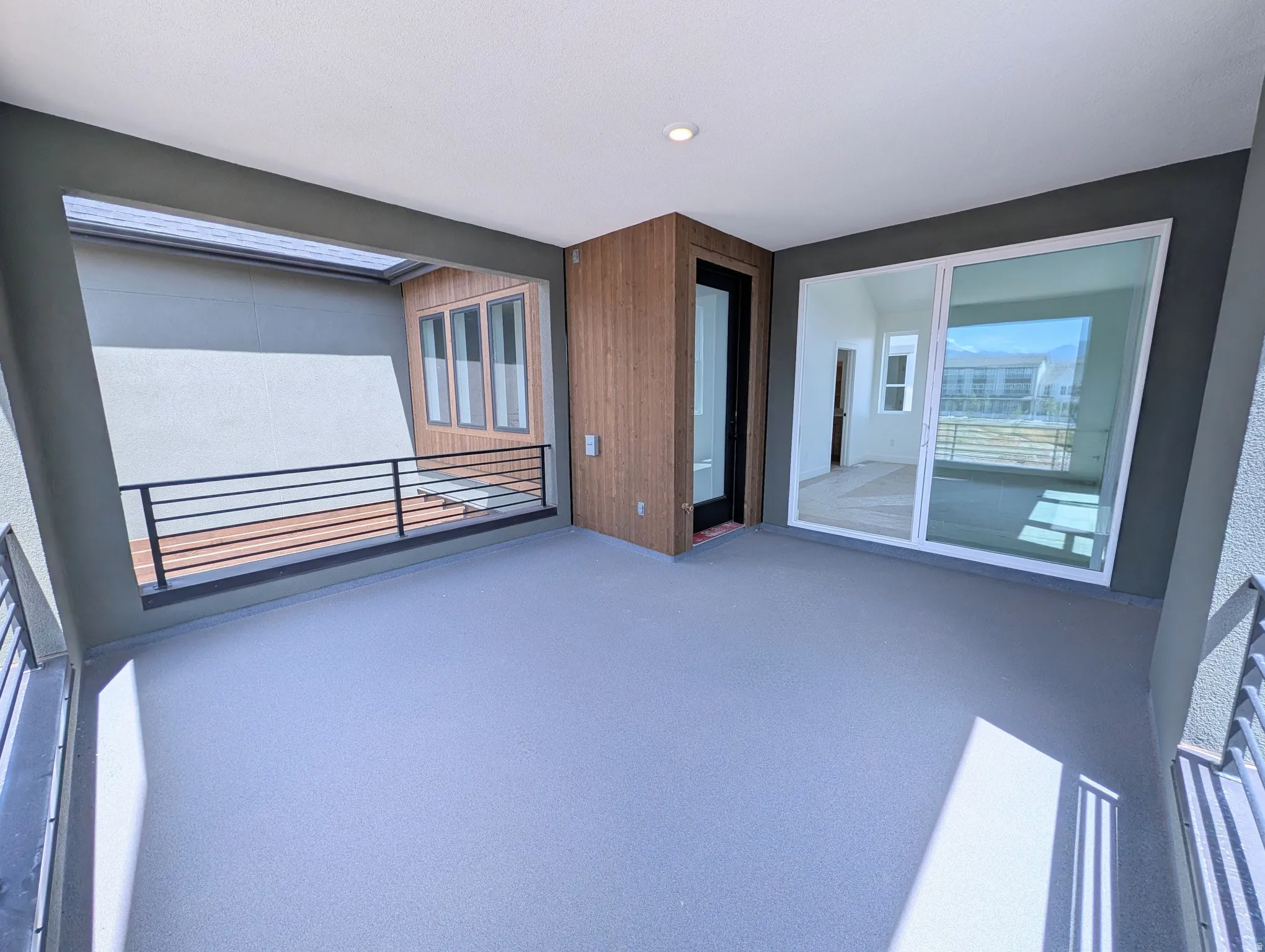 Expansive outdoor patio featuring a neutral-toned flooring surface, a black metal railing, and a wood-paneled exterior wall