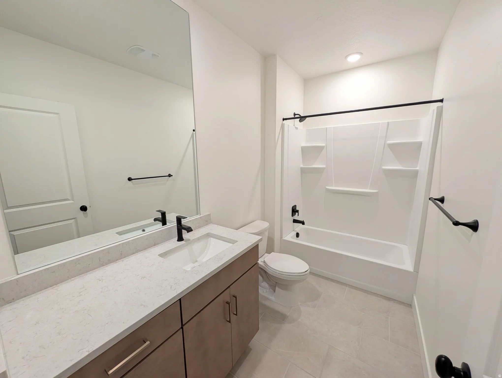 Bathroom featuring a shower/tub combination with integrated shelving, matte black fixtures, a floating vanity with a single basin, a light-toned countertop, and a large wall-mounted mirror