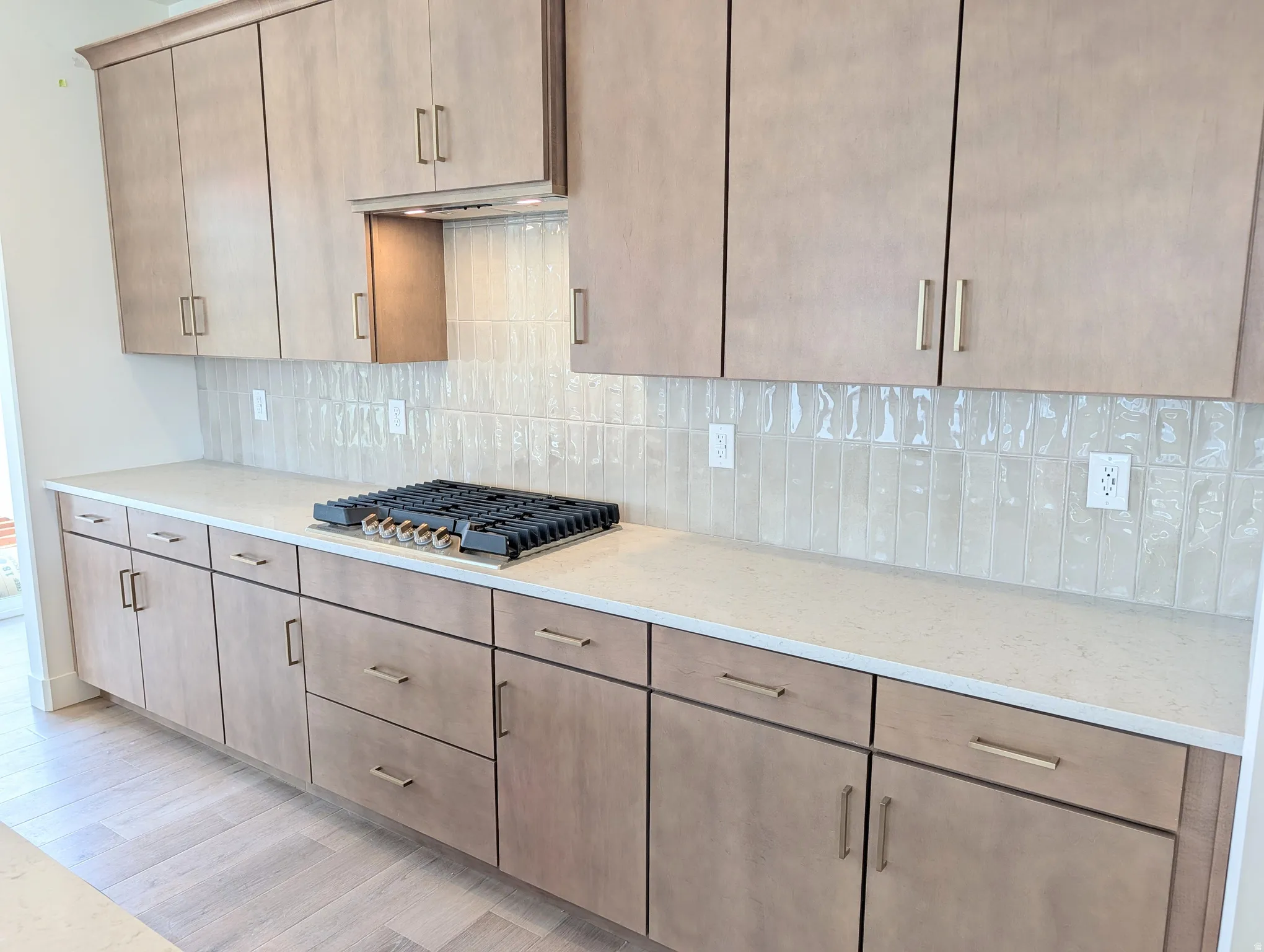 Contemporary kitchen featuring light wood-finish cabinetry, a built-in gas cooktop, quartz countertops, a matching backsplash, and recessed lighting