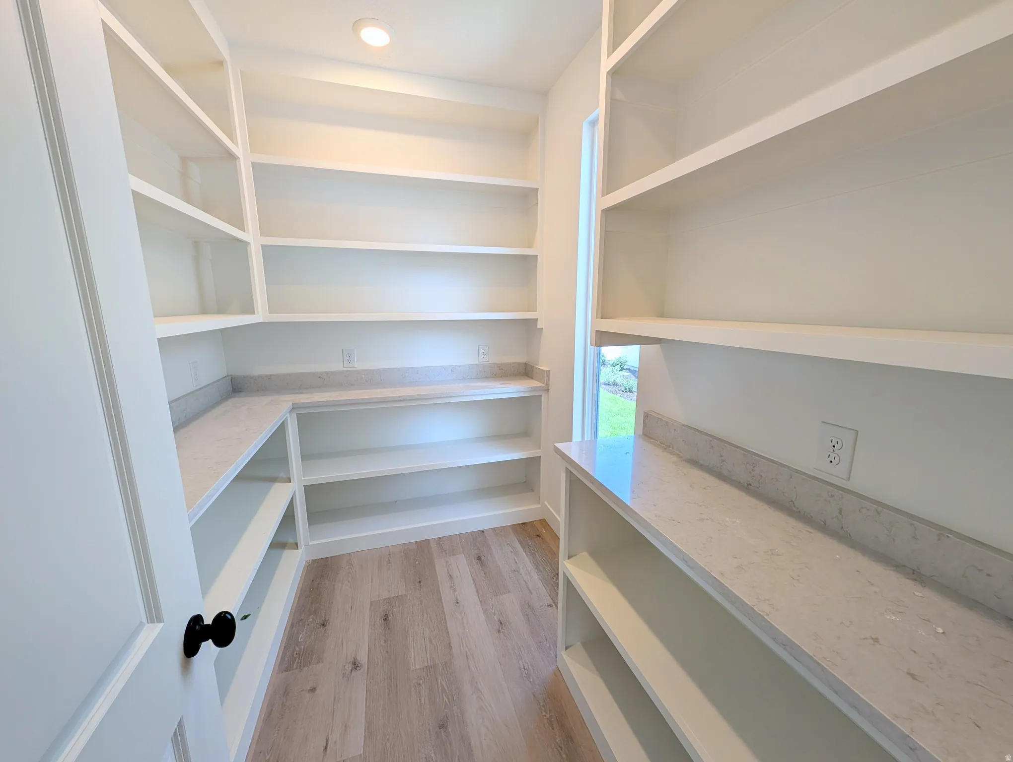 Spacious pantry featuring extensive built-in shelving, light wood-finish flooring, recessed ceiling lighting, and quartz countertops with a matching backsplash