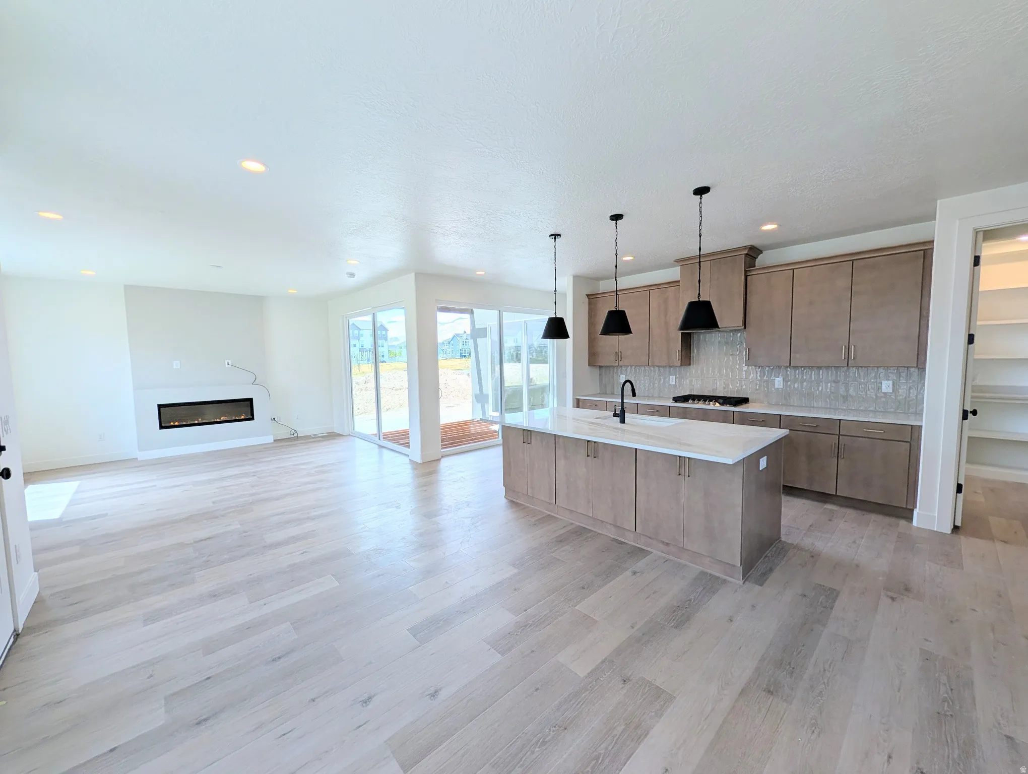 Open-concept living space featuring wood-finish flooring, a linear electric fireplace, and sliding glass doors to the exterior