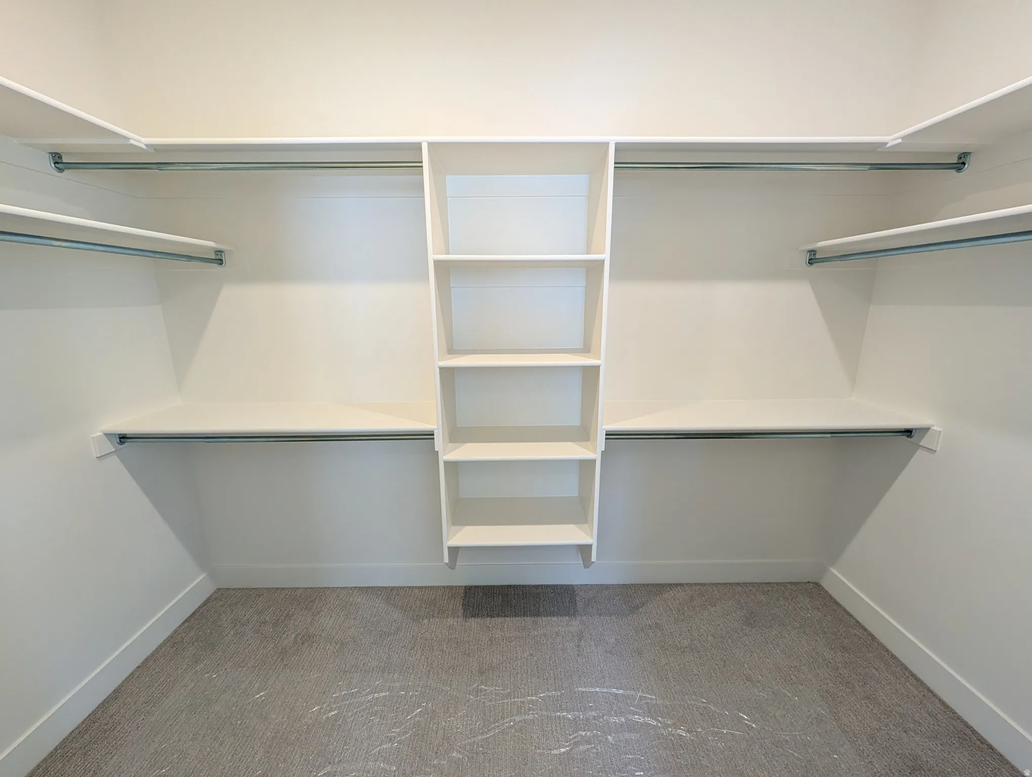 Walk-in closet featuring built-in shelving, multiple hanging rods, and light-colored carpeting