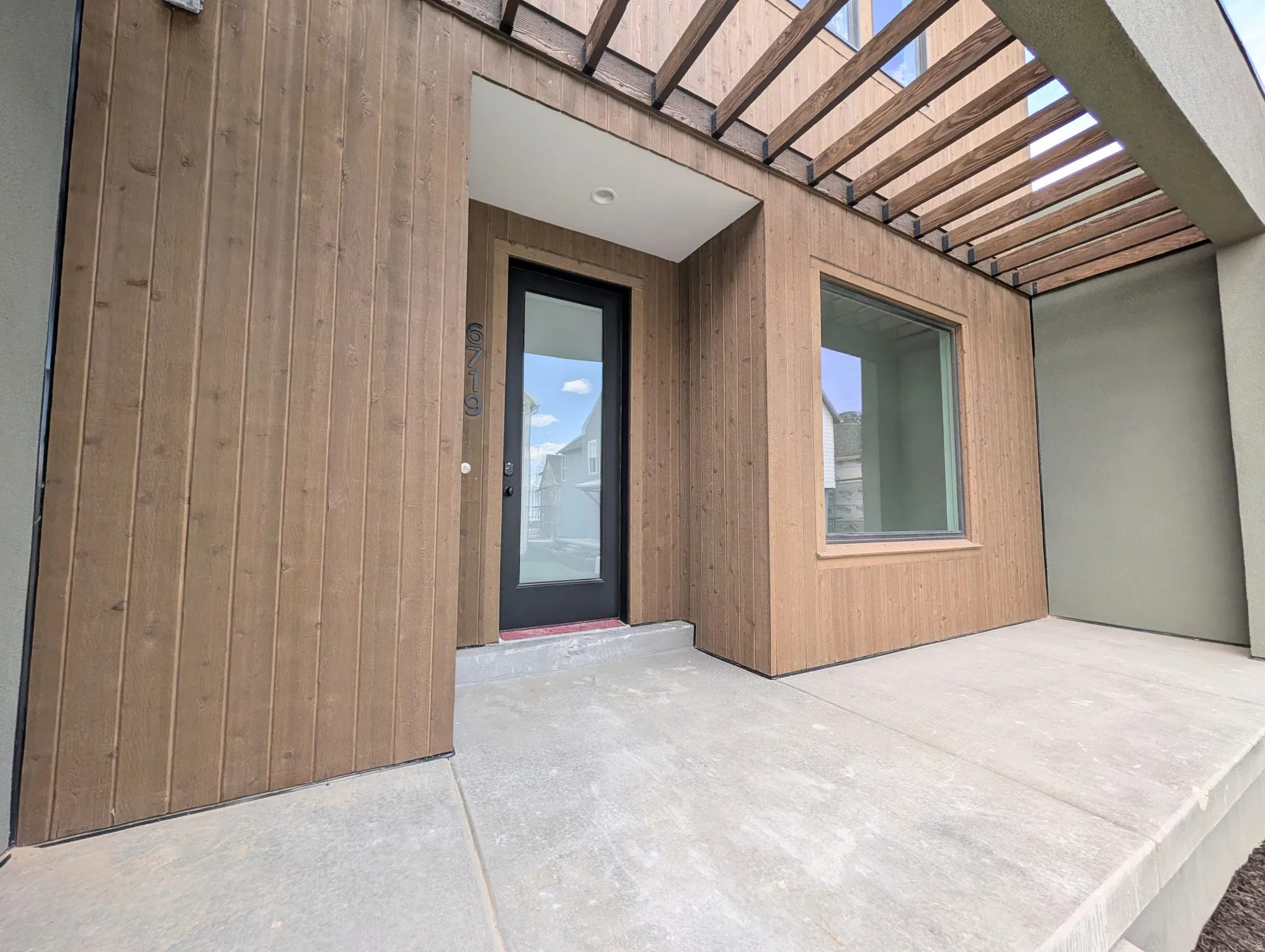 Modern exterior featuring a prominent wood-panel facade, a black-framed glass entry door, and a horizontal wood pergola