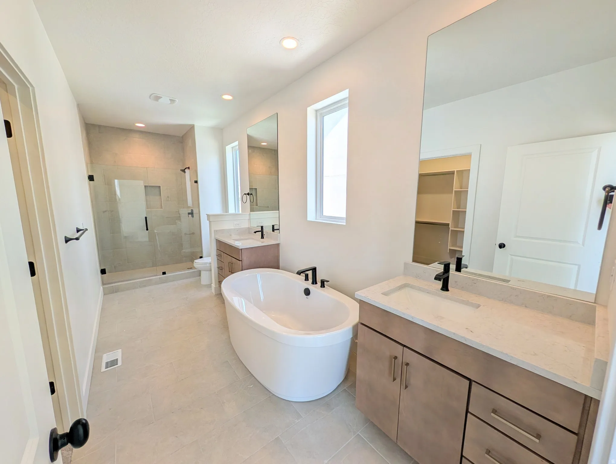 Spacious bathroom featuring a freestanding soaking tub, a large glass-enclosed shower with tile surround, and dual vanities with light-colored countertops