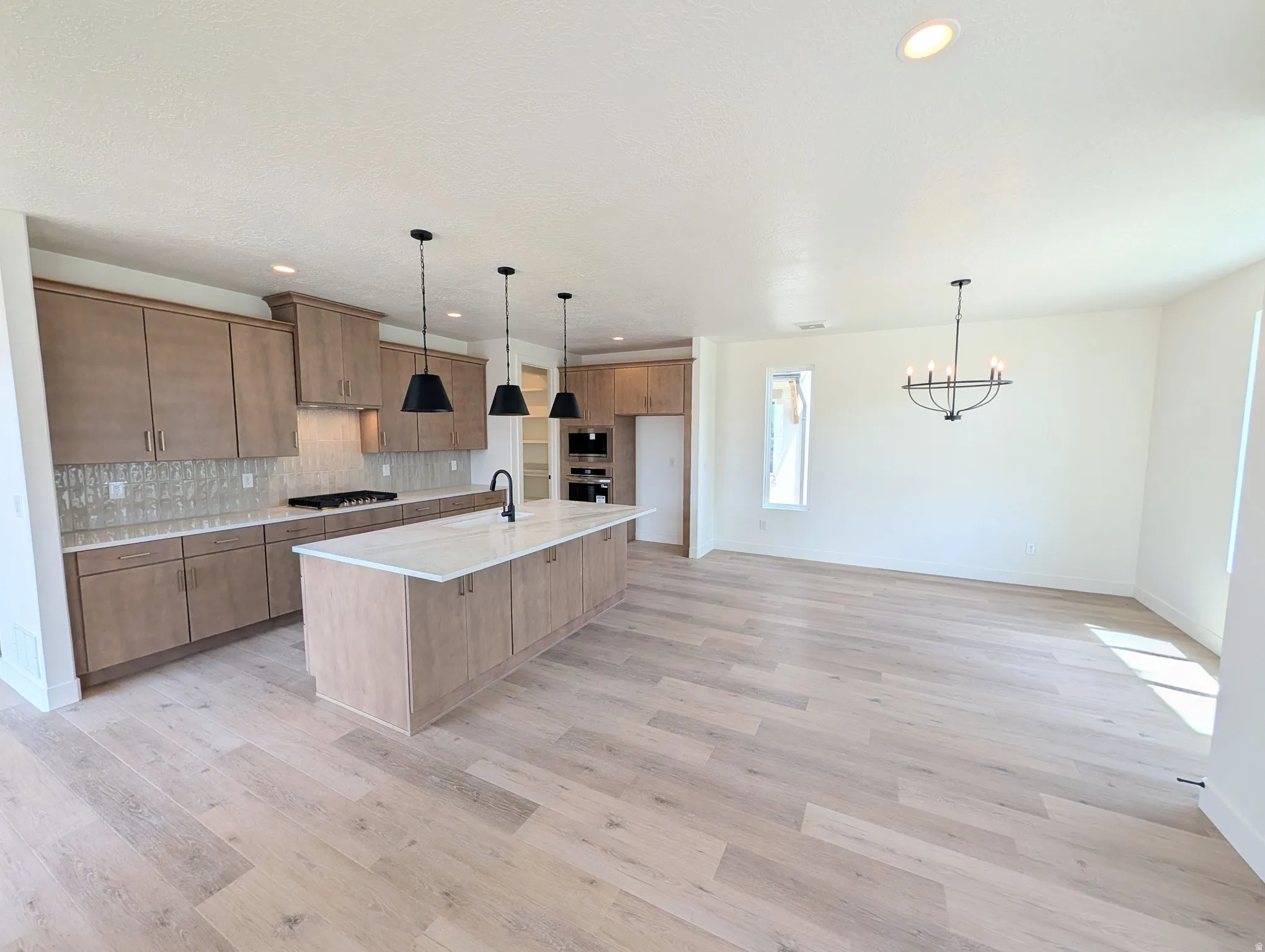 Open-concept living space featuring a kitchen with light wood-finish cabinetry, a large kitchen island with a white countertop, and a tile backsplash