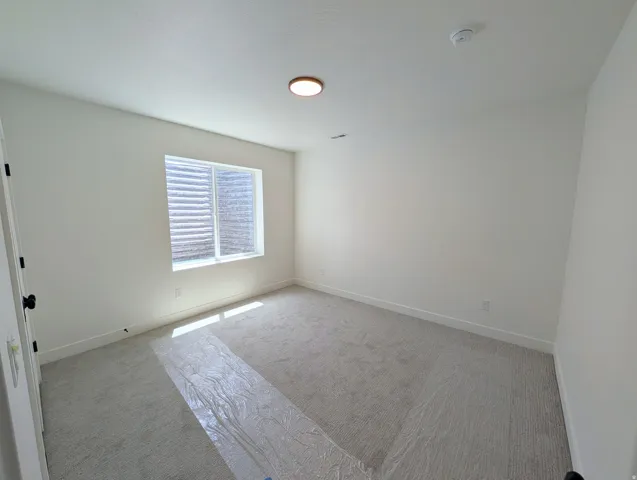 Neutral-toned room featuring a single window with horizontal blinds, light-colored carpeting, a ceiling-mounted light fixture, and white painted walls