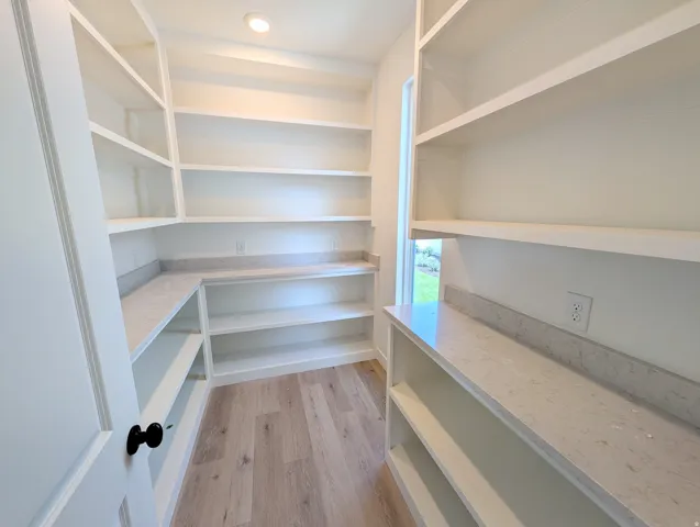 Spacious pantry featuring extensive built-in shelving, light wood-finish flooring, recessed ceiling lighting, and quartz countertops with a matching backsplash
